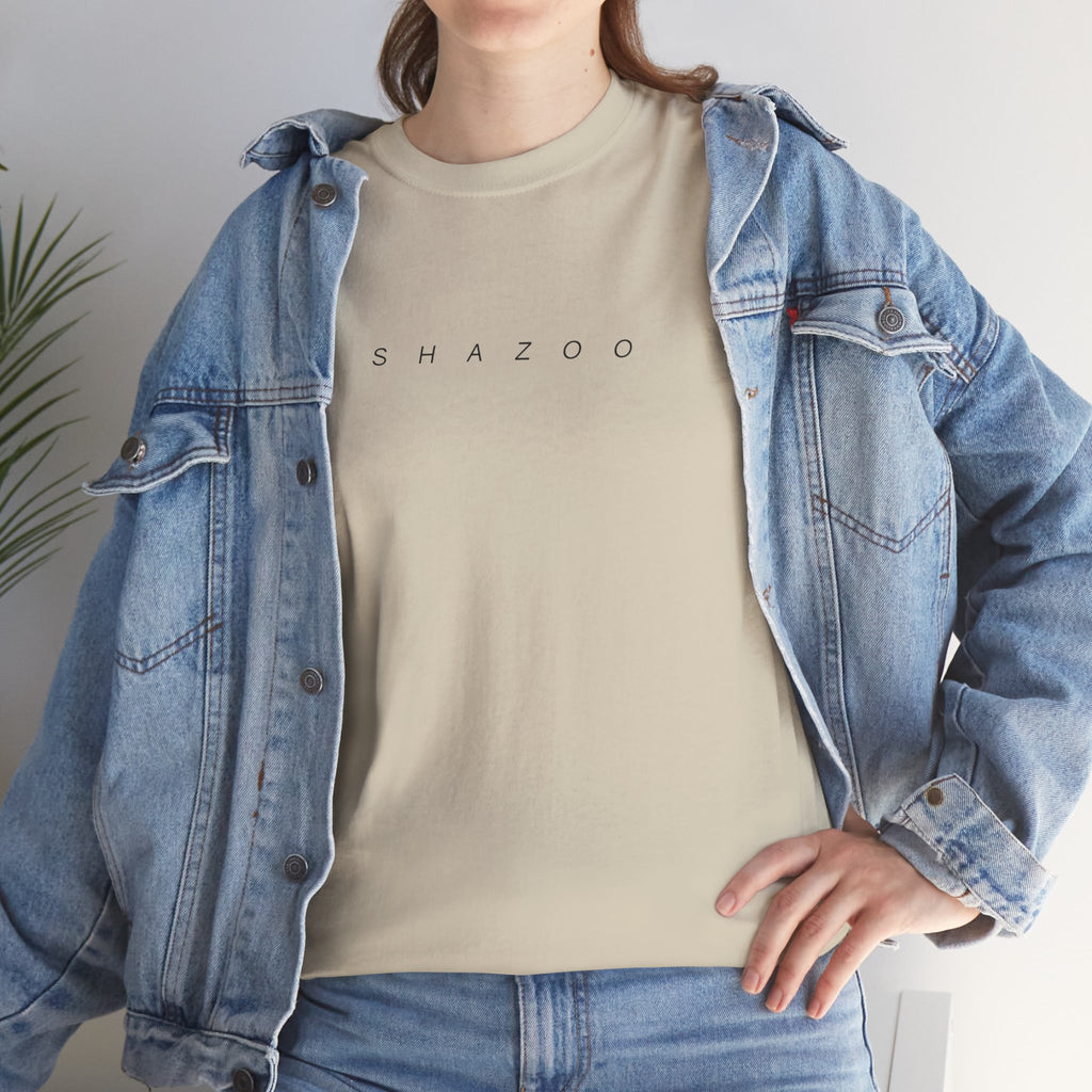 Person wearing a beige t-shirt with 'SHAZOO' text and a denim jacket indoors.